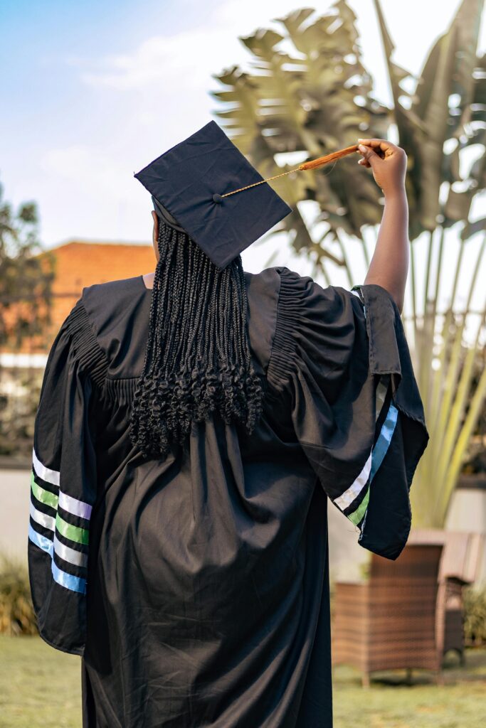 Outdoor shot of a graduate in cap and gown celebrating with diploma raised.